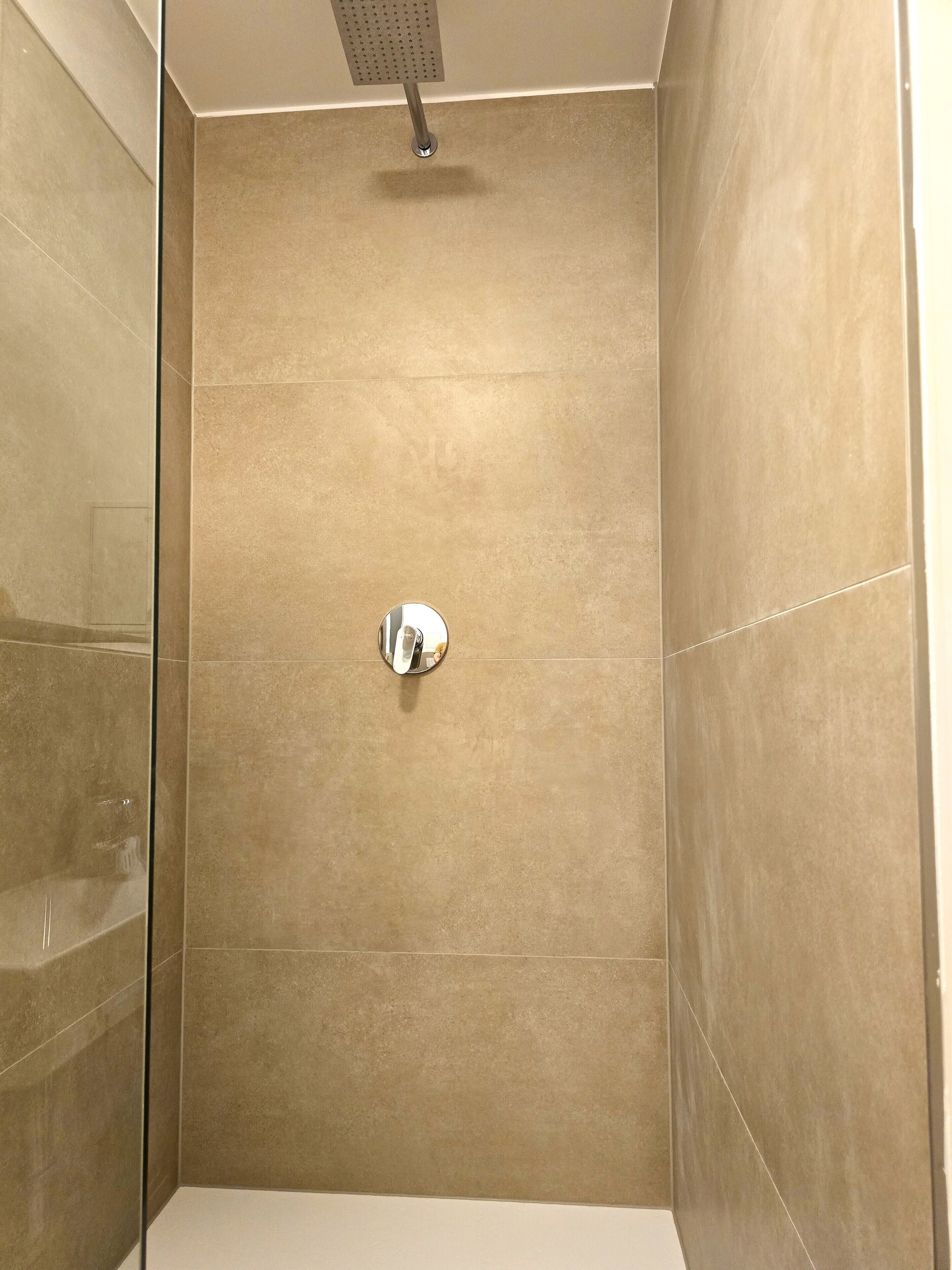 Une douche avec une porte en verre et un pommeau de douche amovible.