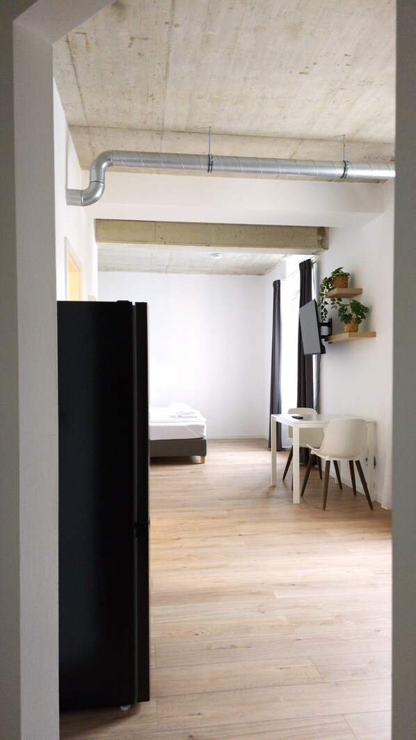 Una habitación pequeña con cama, escritorio, silla y un refrigerador negro.