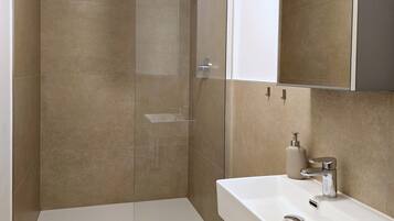 A modern bathroom with a glass-enclosed shower, a white sink, and a large mirror.