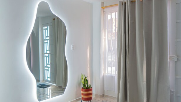 A modern interior with a unique mirror design, a potted plant, and a window with curtains. - Lovely 4-bed House in Palmira Valle del Cauca (Palmira)