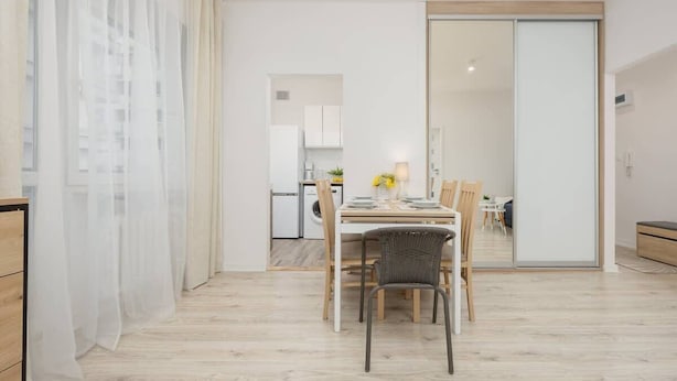 Uma área de jantar moderna com uma mesa de madeira, cadeiras e uma cozinha ao fundo.
