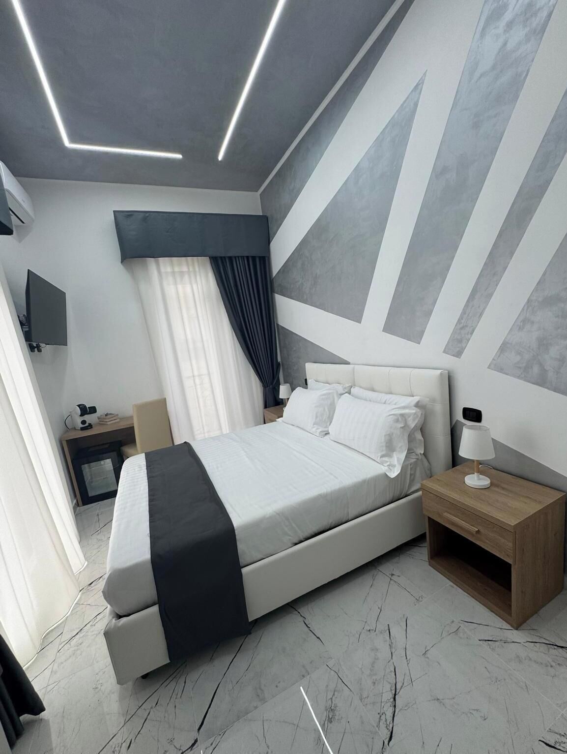 Une chambre moderne avec un lit, des tables de chevet, un téléviseur et un mur orné de motifs géométriques.