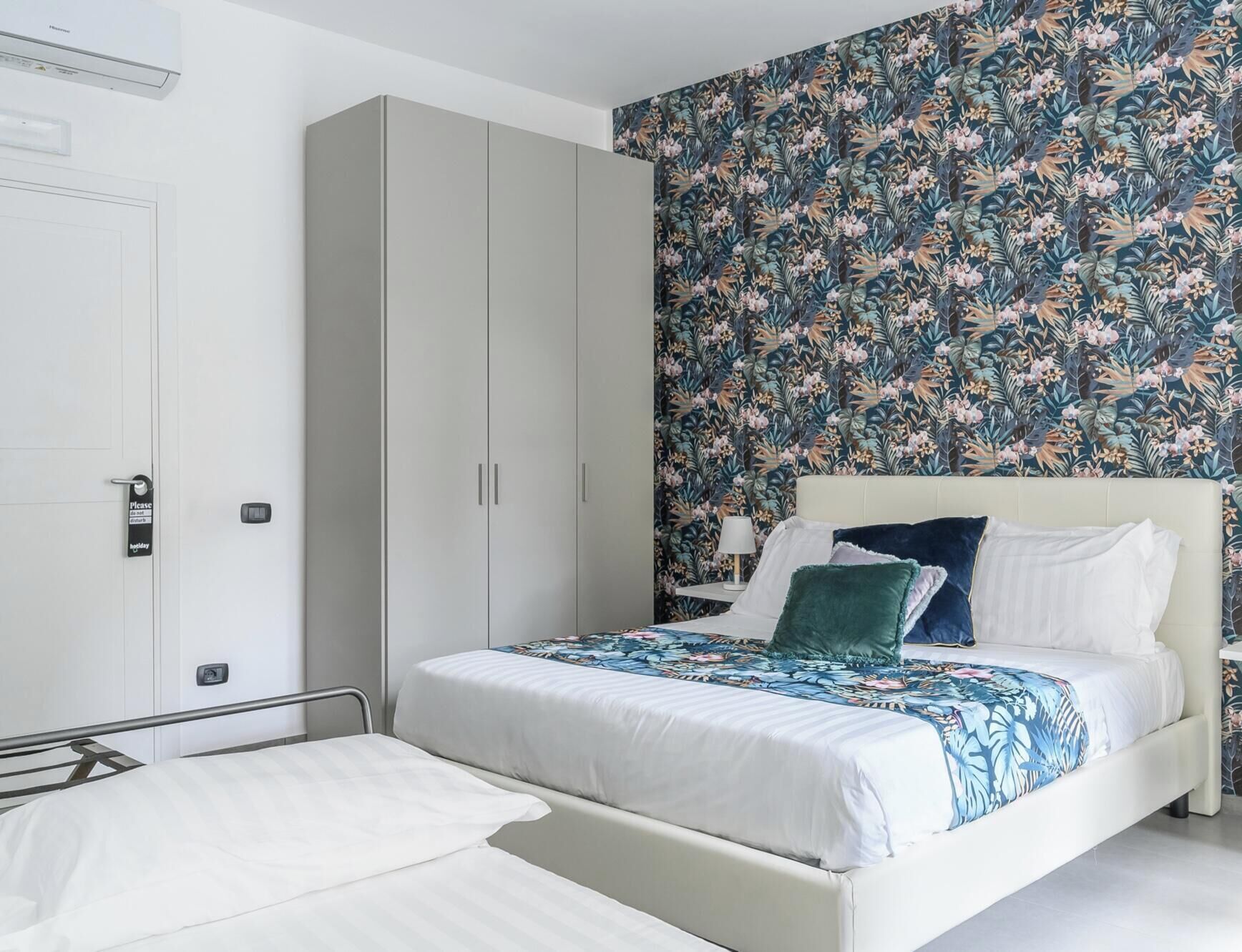 A hotel room with a bed, a wardrobe, a nightstand, and a floral wallpaper.