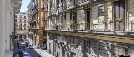 Una calle estrecha flanqueada por edificios de varios pisos, algunos con balcones y macetas.