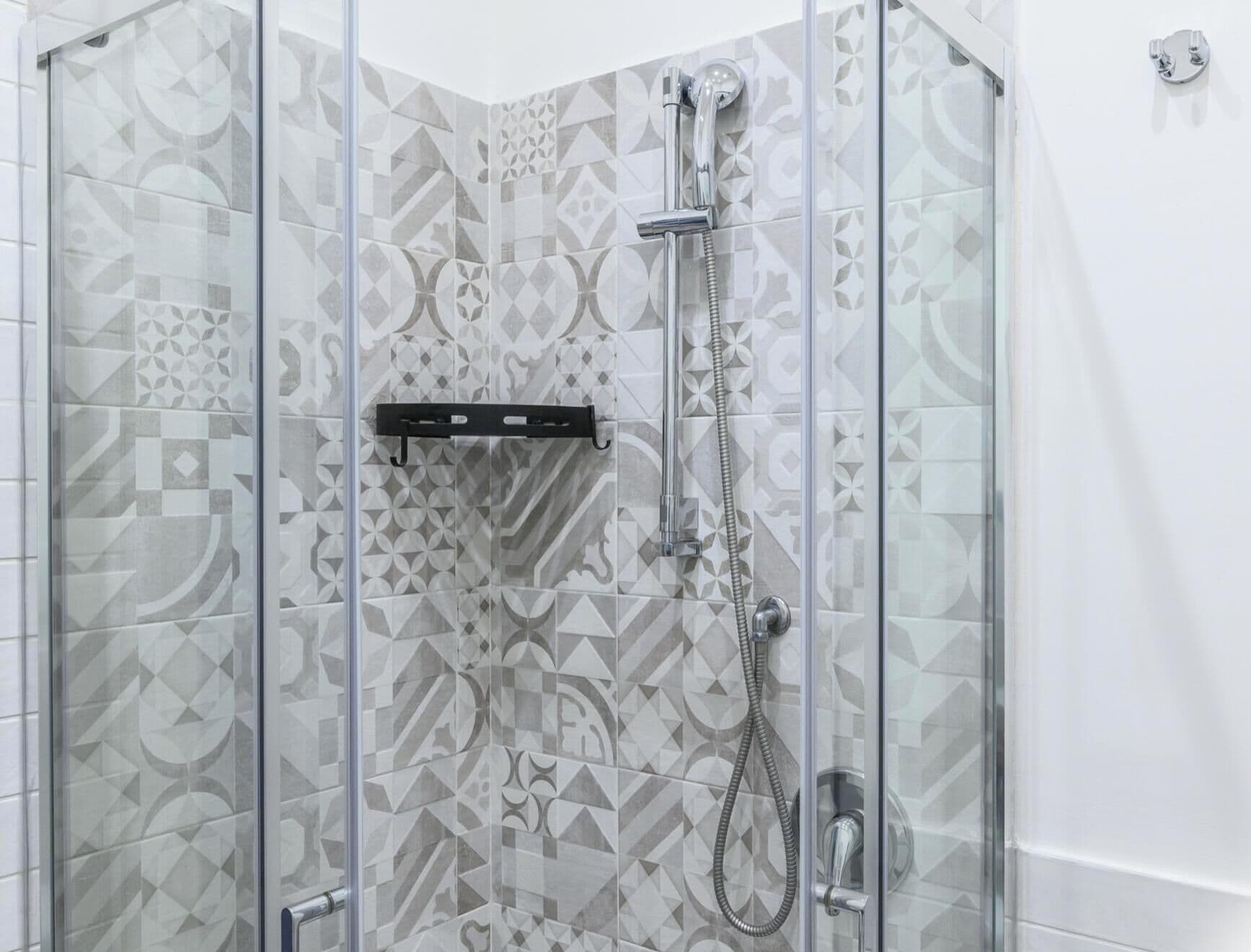 A glass-enclosed shower with a geometric tile pattern on the walls.
