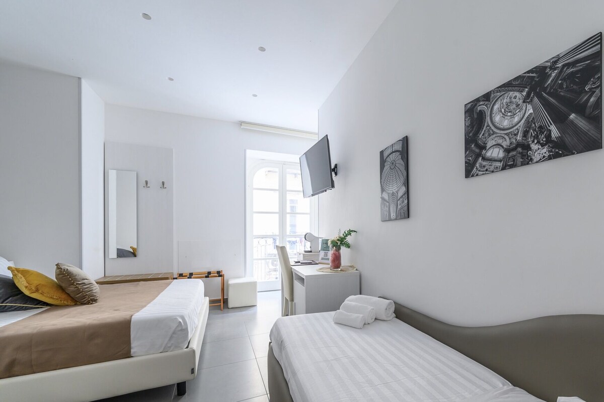 A modern hotel room with two beds, a desk, a TV, and artwork on the walls.