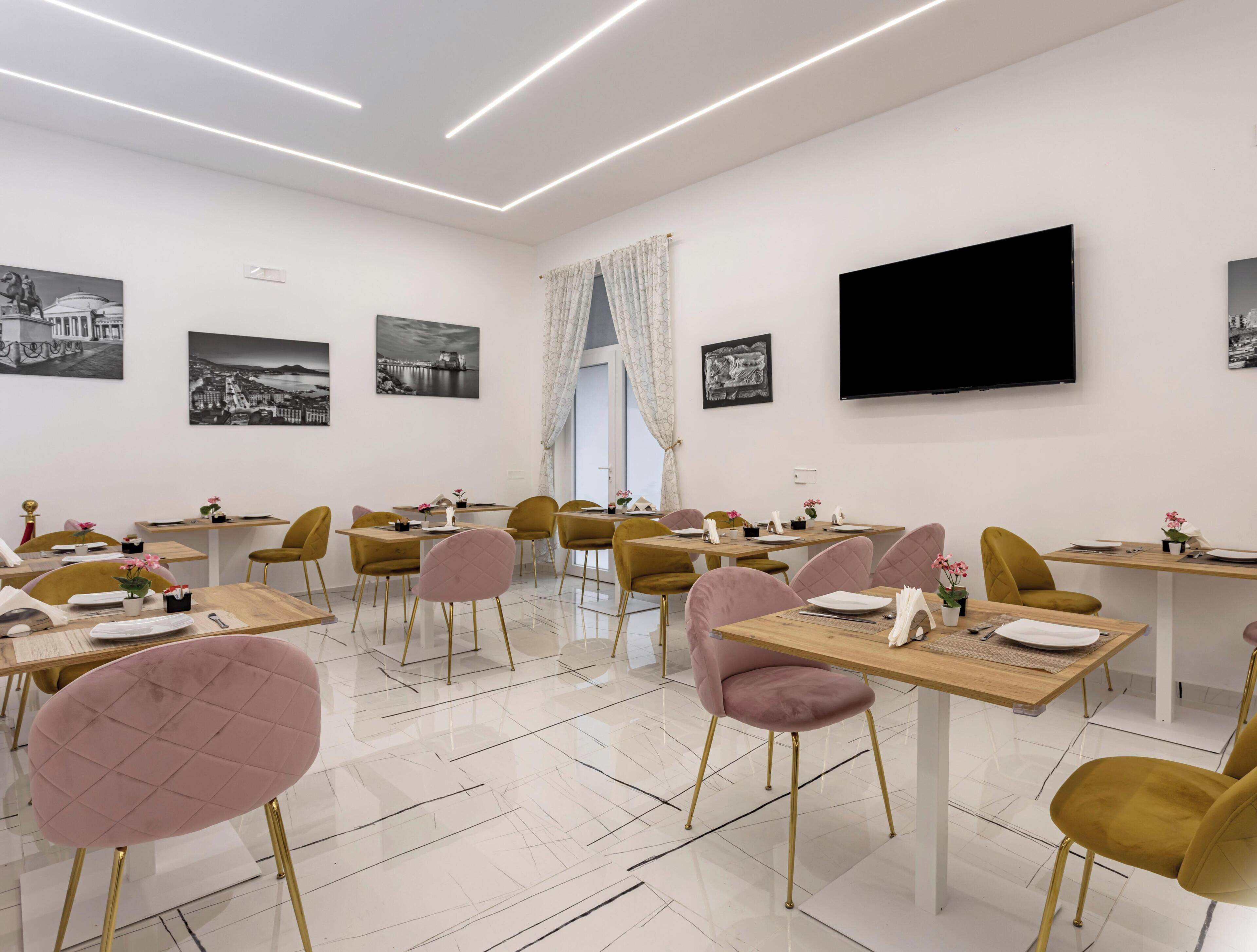 Un espace repas moderne avec plusieurs tables et chaises, un téléviseur à écran plat fixé au mur et des œuvres d’art en noir et blanc qui décorent les murs.