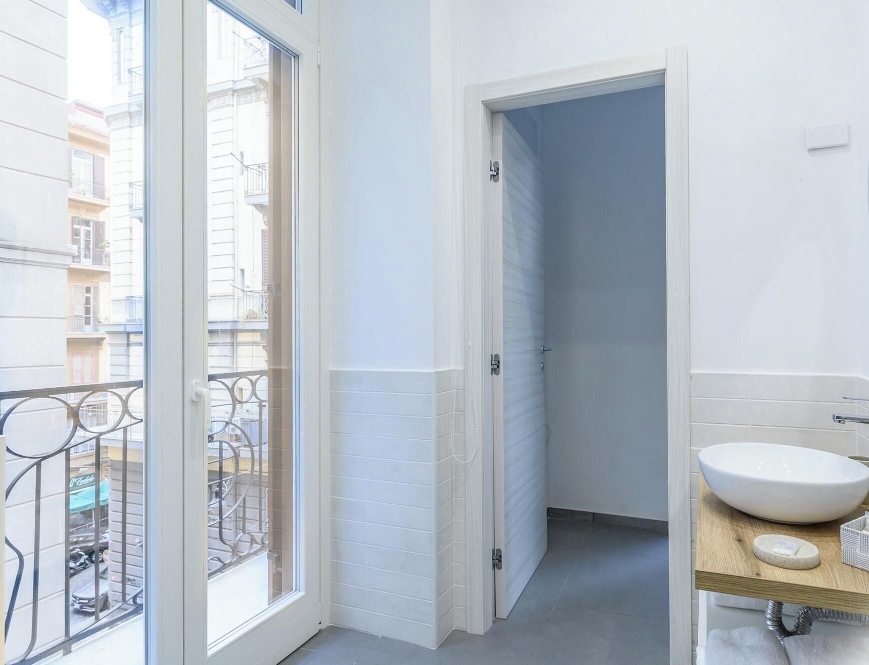 Een badkamer met een wit wastafelmeubel, een houten aanrechtblad en uitzicht op een balkon met metalen hekwerk.