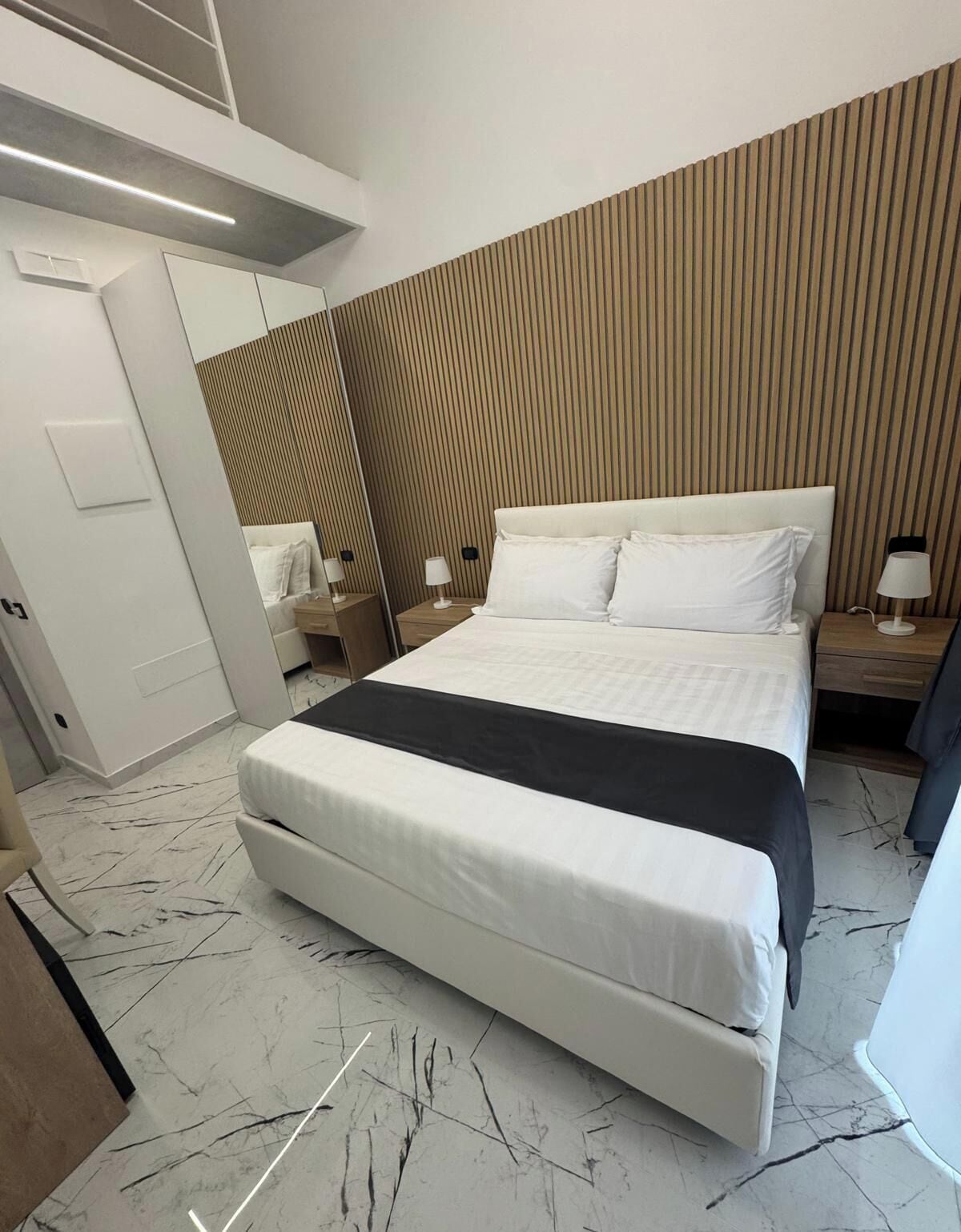 Une chambre d’hôtel moderne avec un grand lit, un mur recouvert de panneaux en bois et un sol en marbre.