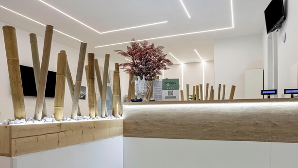 A reception desk with a wooden finish, a vase with flowers, and a sign with a QR code. - Hotiday Room Collection - Napoli Sant’Arcangelo  (Naples)