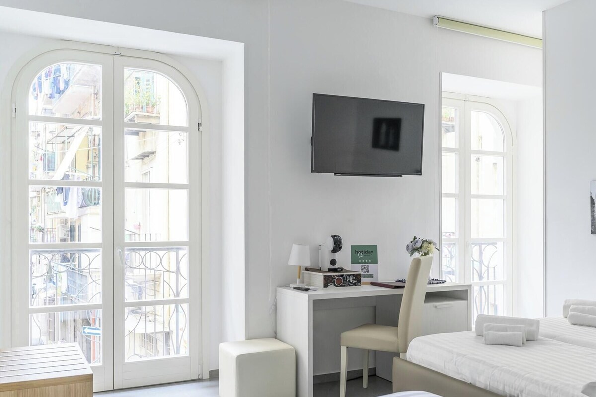A modern hotel room with a desk, chair, bed, and a TV mounted on the wall.
