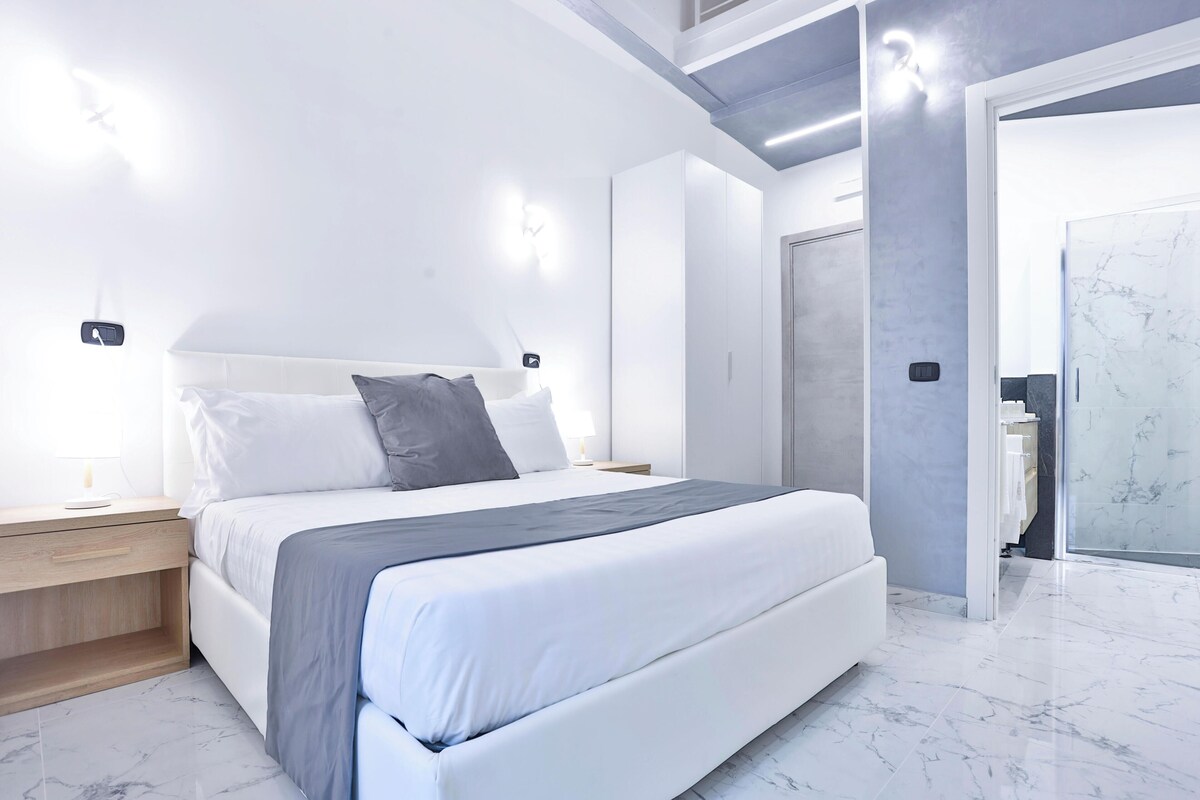A modern bedroom with a large bed, bedside tables, and a wardrobe.