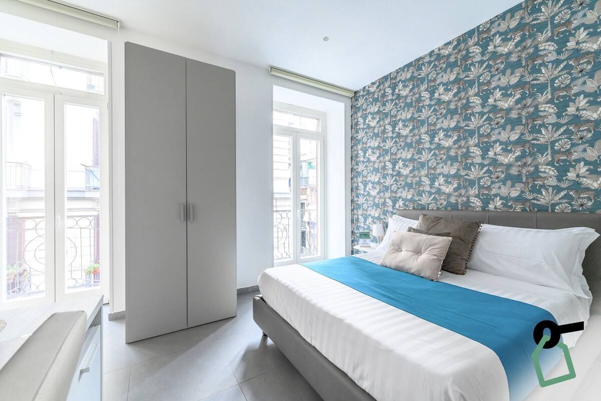 A bedroom with a bed, a wardrobe, and a window with a balcony view.