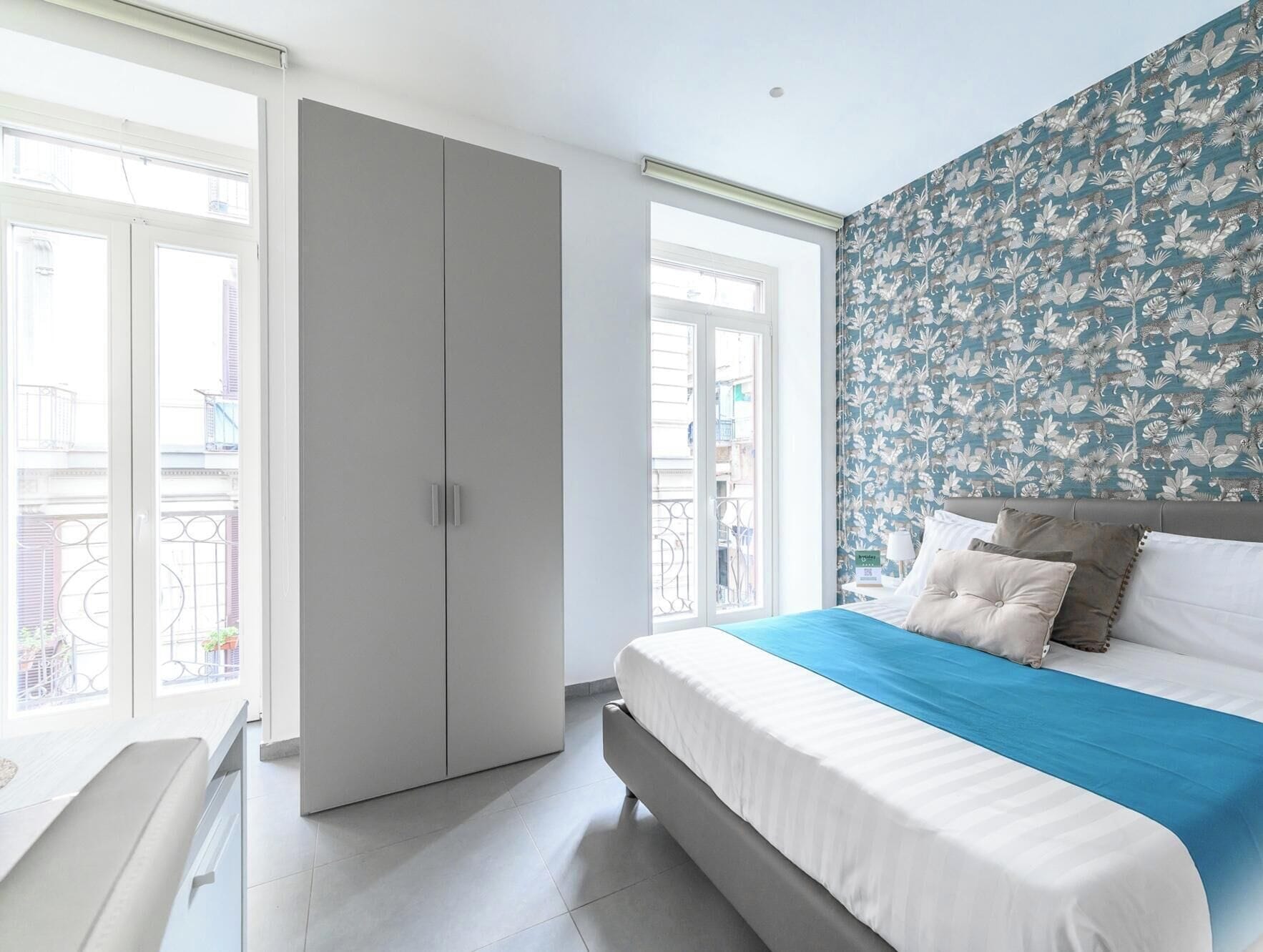 A bedroom with a bed, a wardrobe, and a window with a view of buildings.