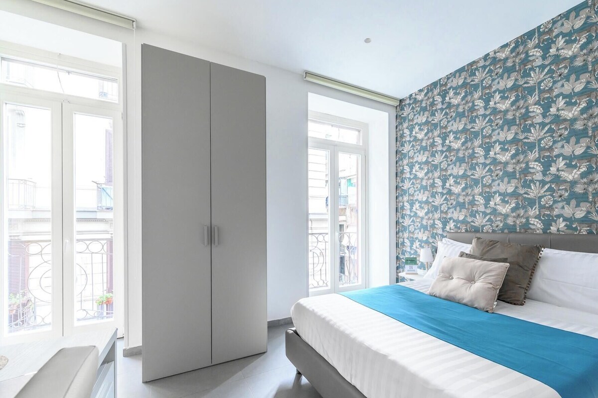 A bedroom with a bed, a wardrobe, and a window with a balcony view.