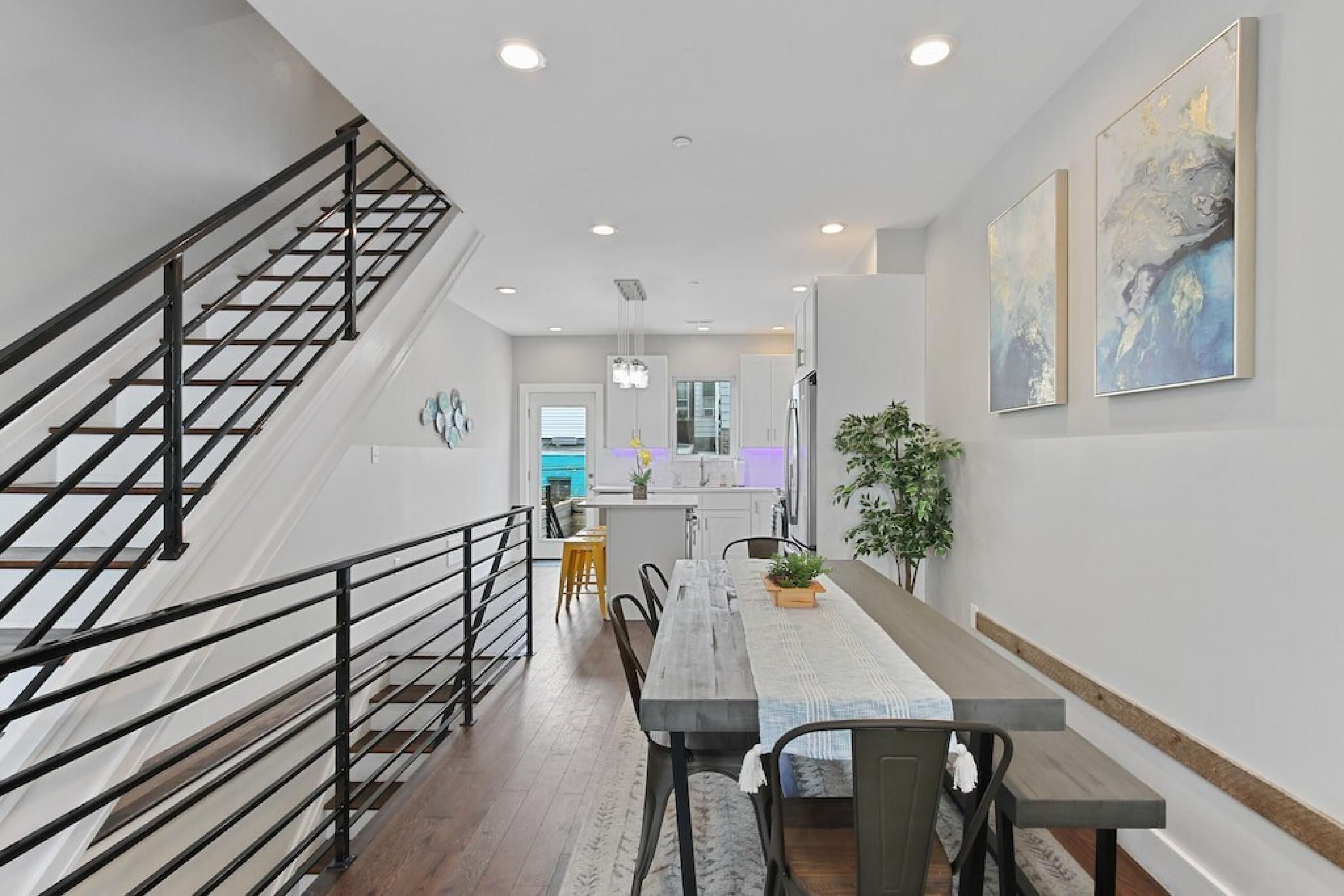A modern kitchen with white cabinets, a central island, and a staircase with black railings.