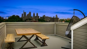 A rooftop patio with a wooden table and benches, a hanging chair, and a city skyline view in the background. - Skyline Best Roofdeck Views 2 Miles Penn Chop (Philadelphia)