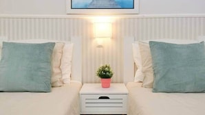 A hotel room with two beds, a nightstand with a lamp, a potted plant, and a framed picture on the wall.