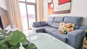A modern living room with a grey sofa, a glass coffee table, and a large window with curtains.