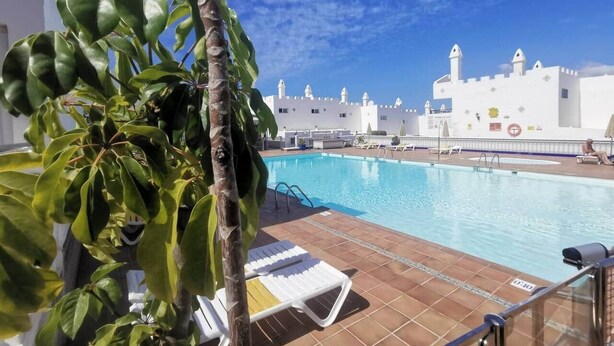 Una piscina con sillas de descanso y un edificio de paredes blancas y torres al fondo.