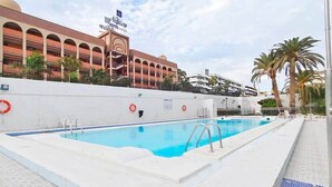 Een zwembad met een reddingsboei, een veiligheidsteken en het hotel Neptun Hotel op de achtergrond.