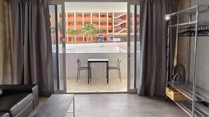 Een moderne kamer met een schuifdeur naar een balkon, een klein tafeltje met stoelen, een stapelbed en een opbergruimte.