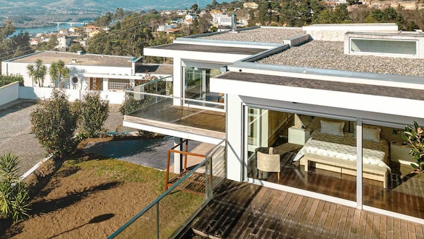 Ein modernes Haus mit einer Holterrasse, einem verglasten Balkon und Blick auf ein Tal.