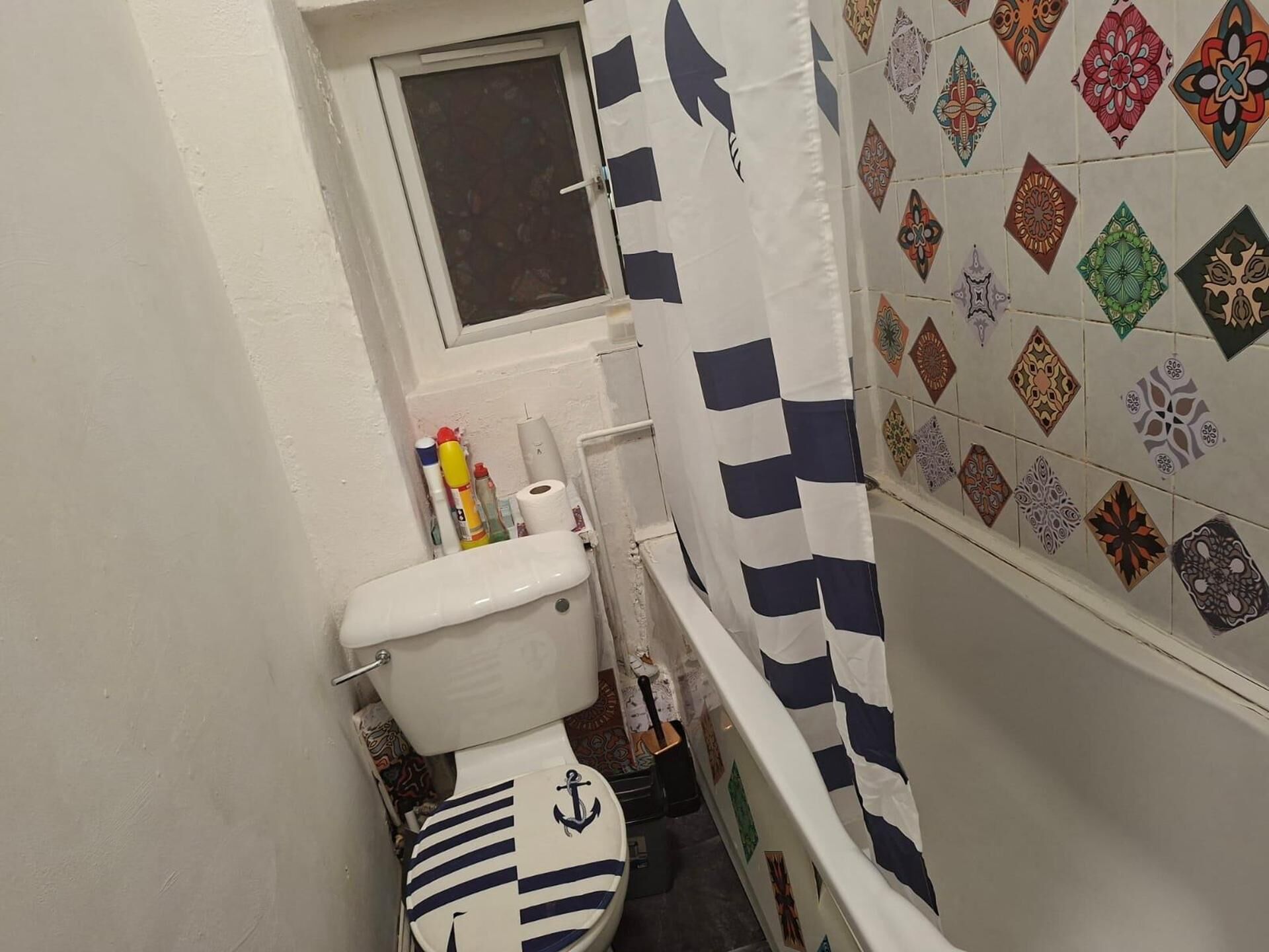 A small bathroom with a toilet, a window above the sink, and a shower curtain with a geometric pattern.