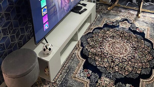 A living room with a large flat-screen TV on a white stand, a patterned rug, a grey armchair, and a wall with a geometric tile design. - Humuplace Sleeps 4 With Garden (Birmingham)