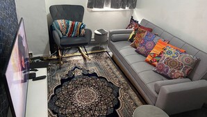 A living room with a grey sofa, colorful cushions, a patterned rug, a black armchair with a multicolored throw, and a TV on a stand. - Humuplace Sleeps 4 With Garden (Birmingham)
