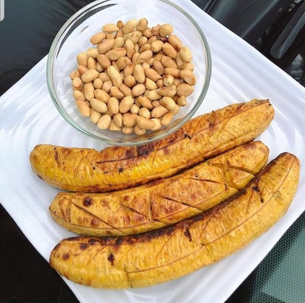 Un plato blanco con plátanos a la parrilla y un tazón de cacahuates.
