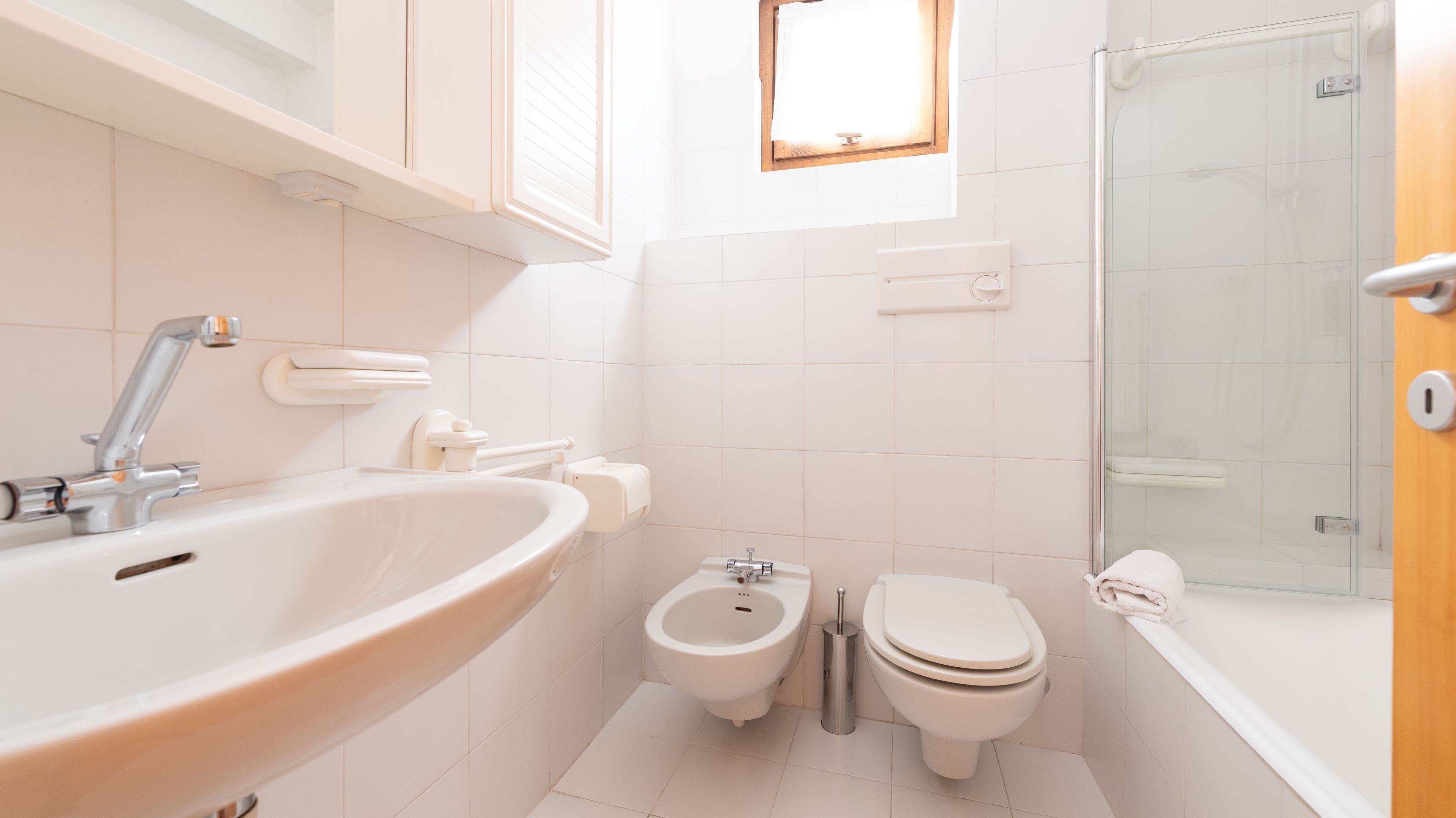 Et lille, moderne badeværelse med håndvask, bidet, toilet og en glasbrusekabine.