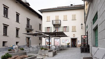Un cortile con posti a sedere all'aperto, una fontana e un edificio con numerose finestre e persiane.
