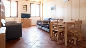 Un salon confortable avec un canapé, une table à manger et des chaises. On y trouve un téléviseur posé sur un meuble et un tableau encadré accroché au mur.