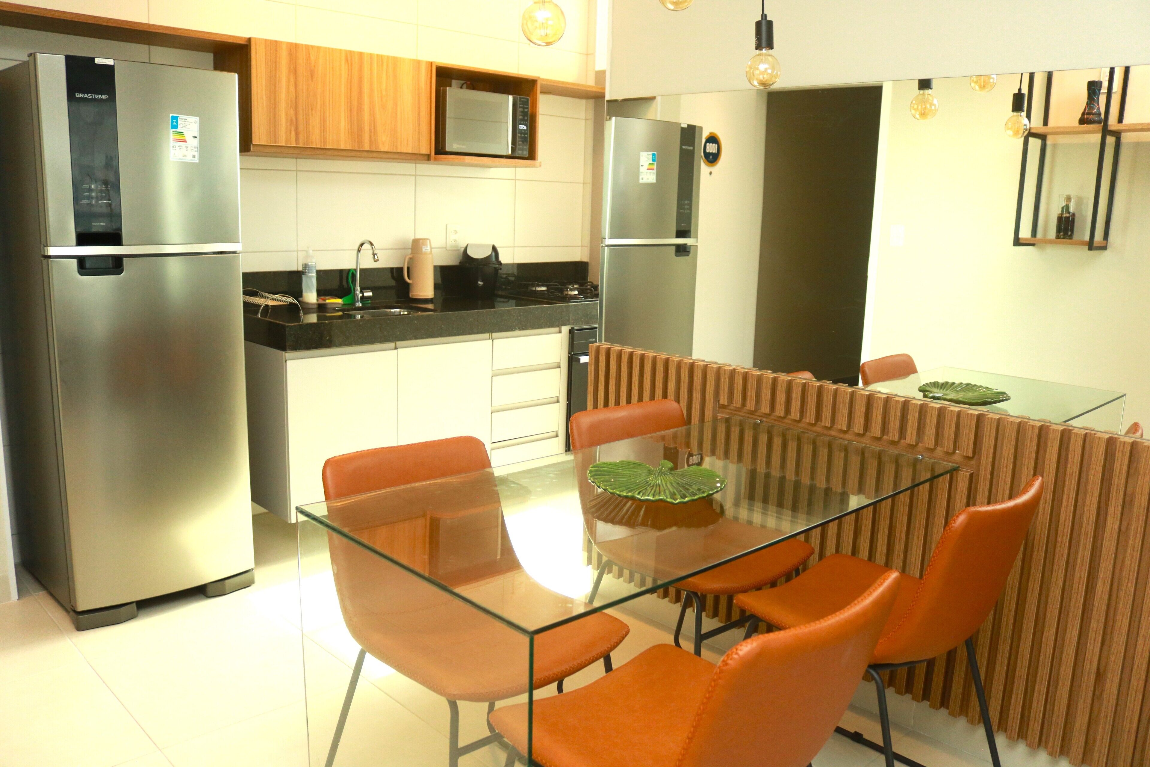 A modern kitchen with stainless steel appliances, a glass dining table, and orange chairs.