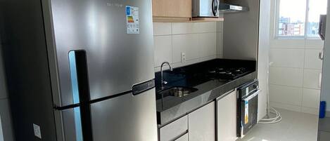Une cuisine moderne dotée d’appareils électroménagers en acier inoxydable, de meubles blancs et d’une fenêtre laissant entrer la lumière naturelle.