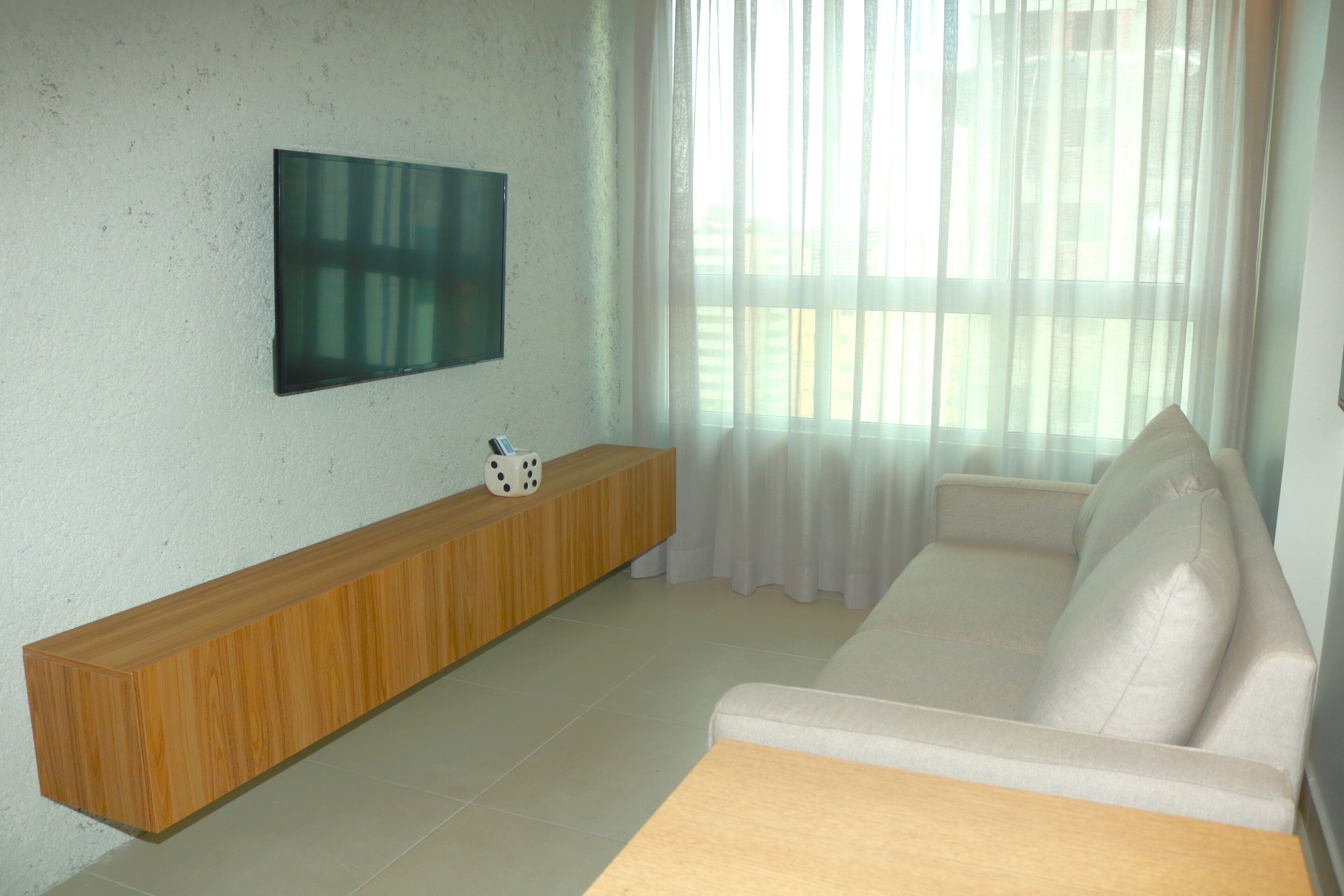 Een woonkamer met een witte bank, een houten salontafel en een flatscreen televisie aan de muur.