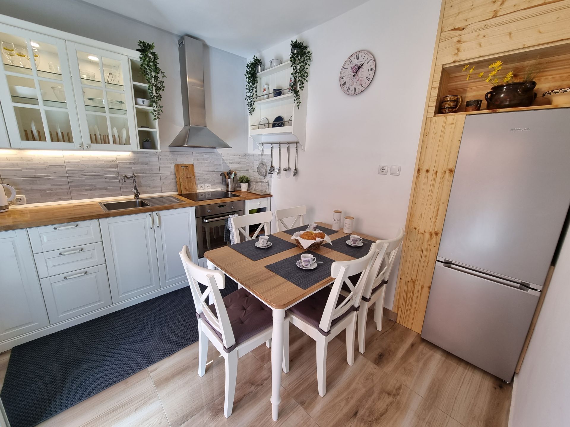 Een moderne keuken met witte kasten, een houten aanrechtblad en een eethoek met een tafel gedekt voor vier personen.