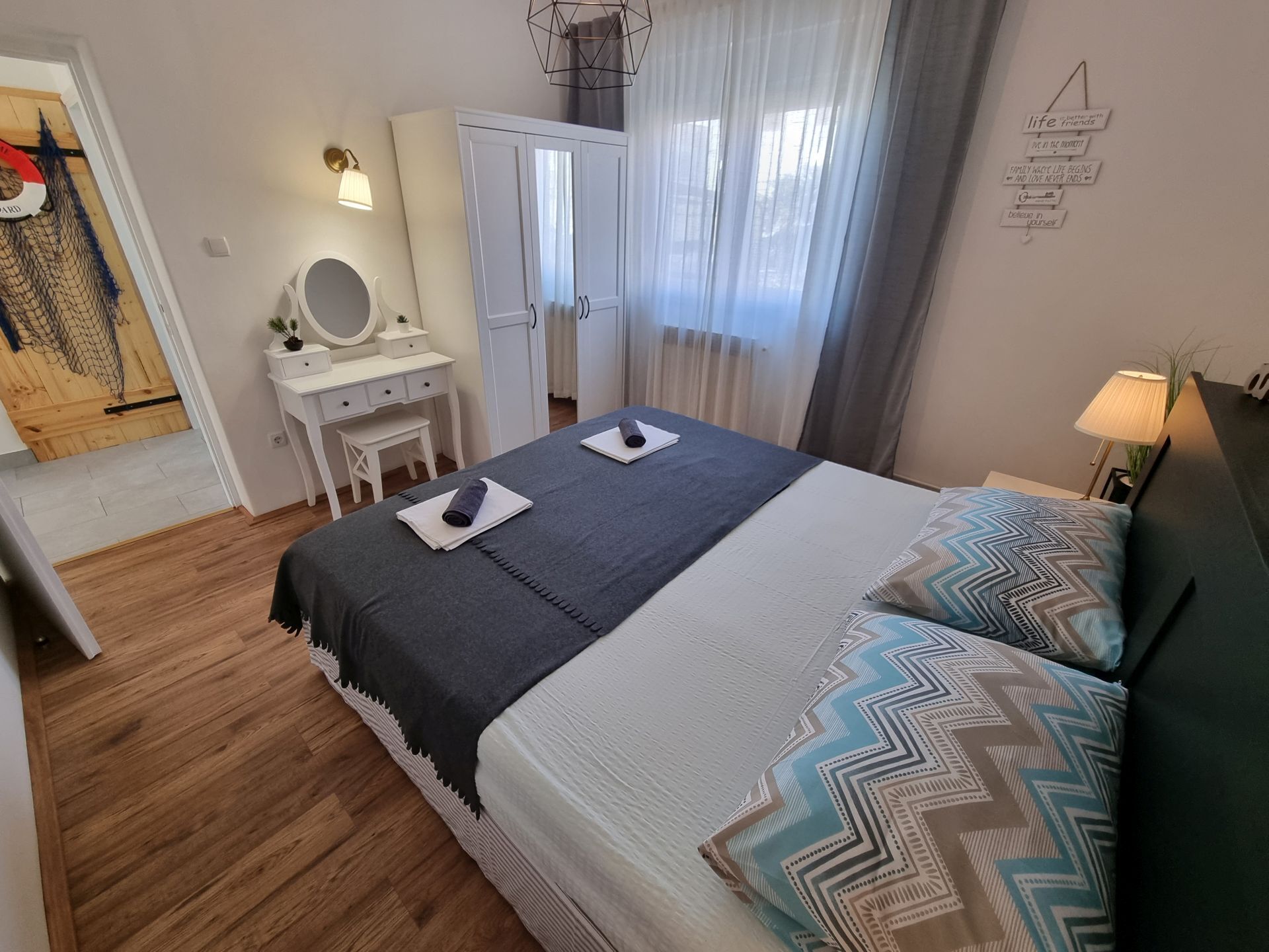 Ein Schlafzimmer mit Bett, Nachttischen, einem Schminktisch, einem Spiegel und einem Fenster mit Vorhängen.