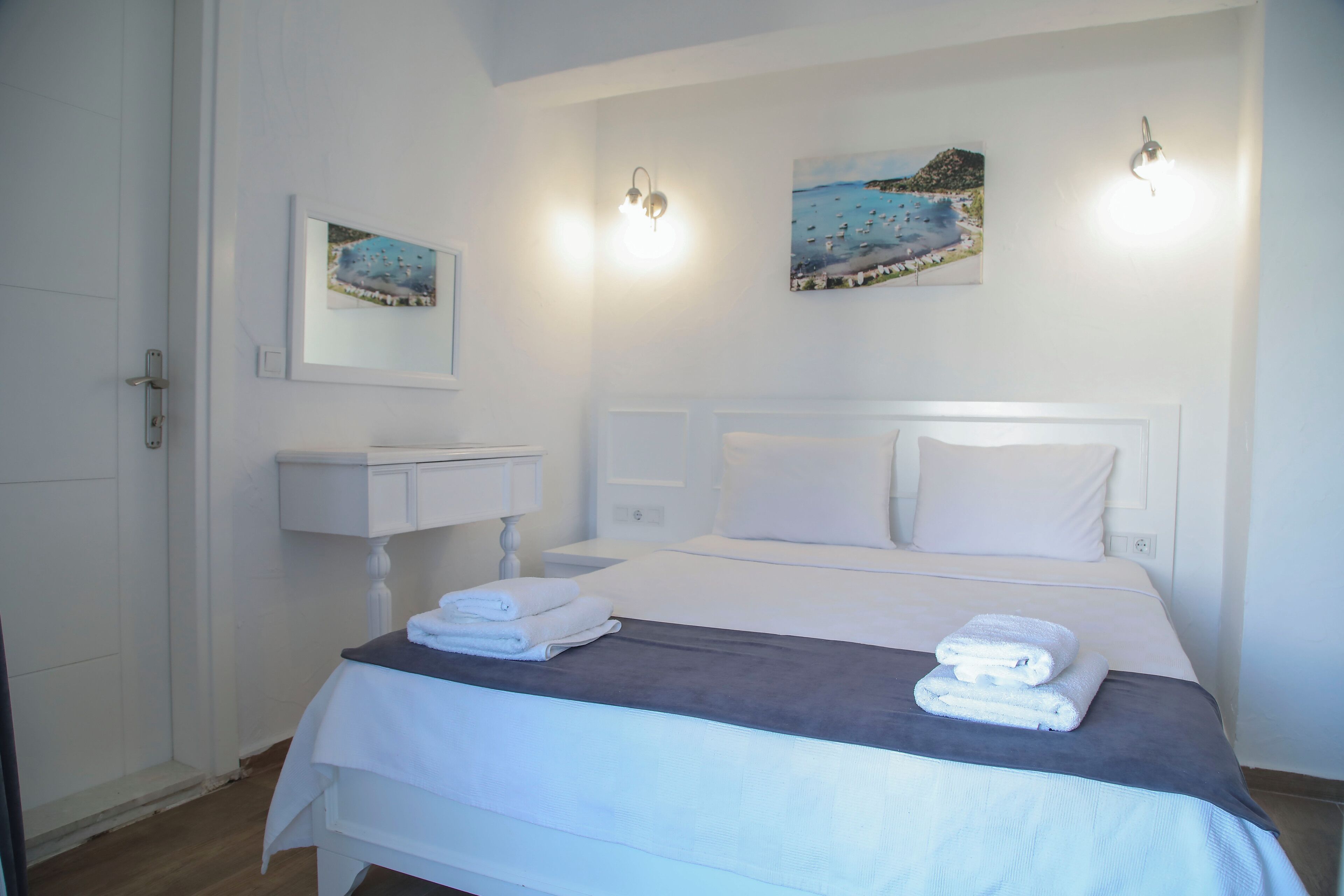 A hotel room with a bed, a nightstand, a white dresser, and two wall-mounted paintings.