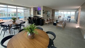 A spacious living area with a kitchen, dining area, and large windows offering a city view. - Edifício Promenade II Apt 907 (Maceió)