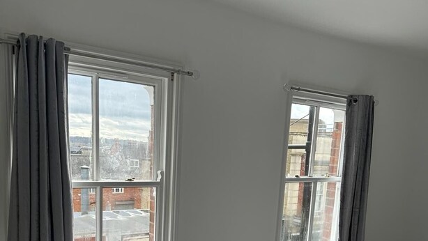 Ein Schlafzimmer mit zwei Fenstern, einem Bett und Blick auf Gebäude.