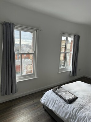 Une chambre avec deux fenêtres, un lit et une vue sur les bâtiments environnants.
