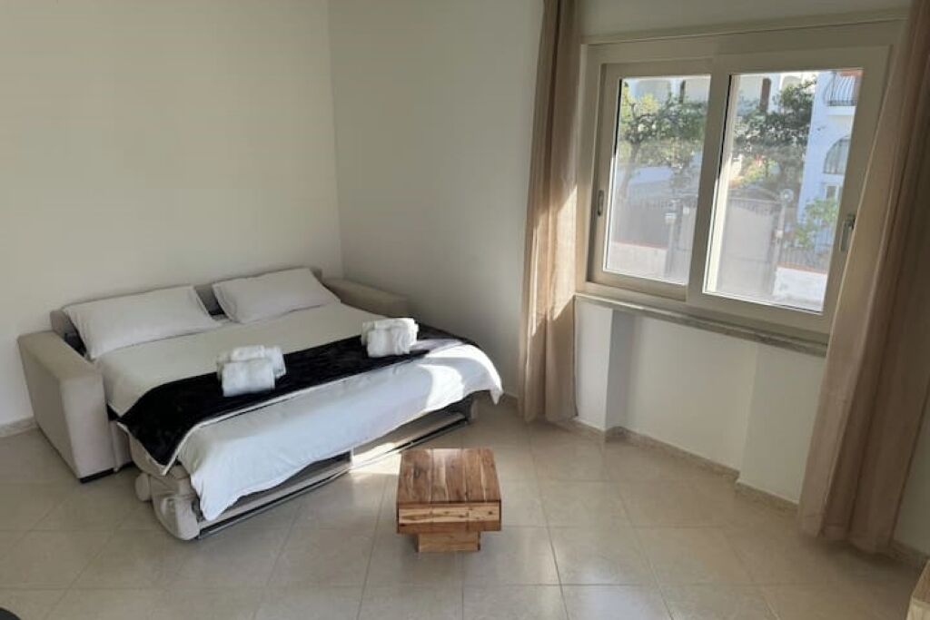 A bedroom with a bed, a small wooden table, and a window with curtains.