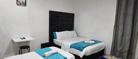 A small, clean room with two beds, a desk, and a chair.