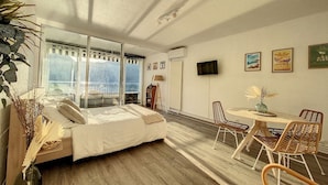 A bedroom with a bed, a dining table with chairs, a TV, and a balcony with a view. - Cosy - Vue Imprenable sur le lac (Tresserve)