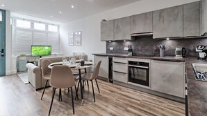 Eine moderne Küche mit Essbereich, ausgestattet mit Backofen, Geschirrspüler und großem Fenster mit Jalousien.