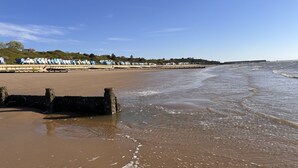 Ein Strand mit sandigem Ufer, einer Steinmauer und einer Reihe Strandhäusern im Hintergrund.