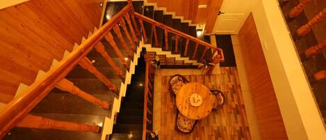 A wooden staircase with a handrail leading to a landing area with a round table and chairs.