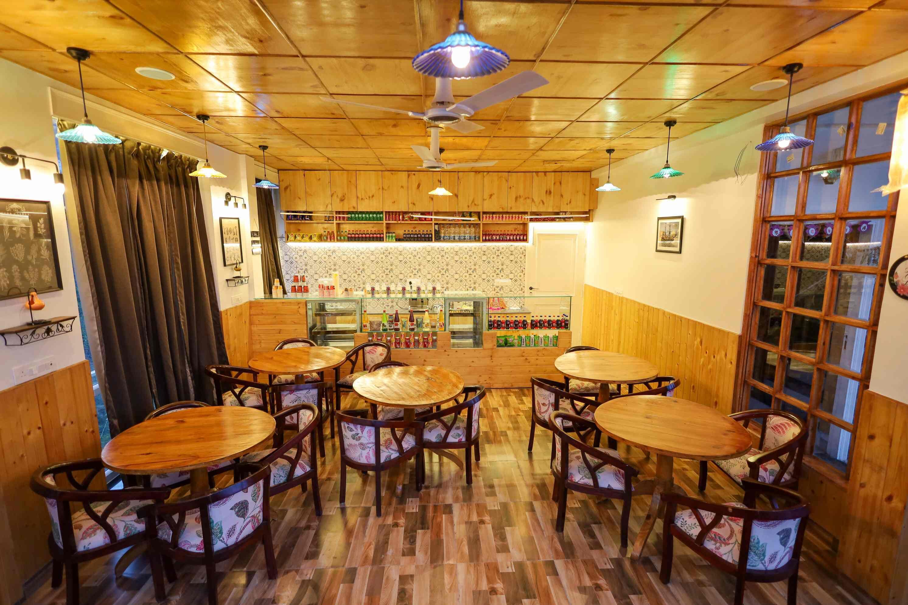 A restaurant interior with wooden floors, round tables, and chairs, a bar area with shelves of bottles, and a ceiling fan.